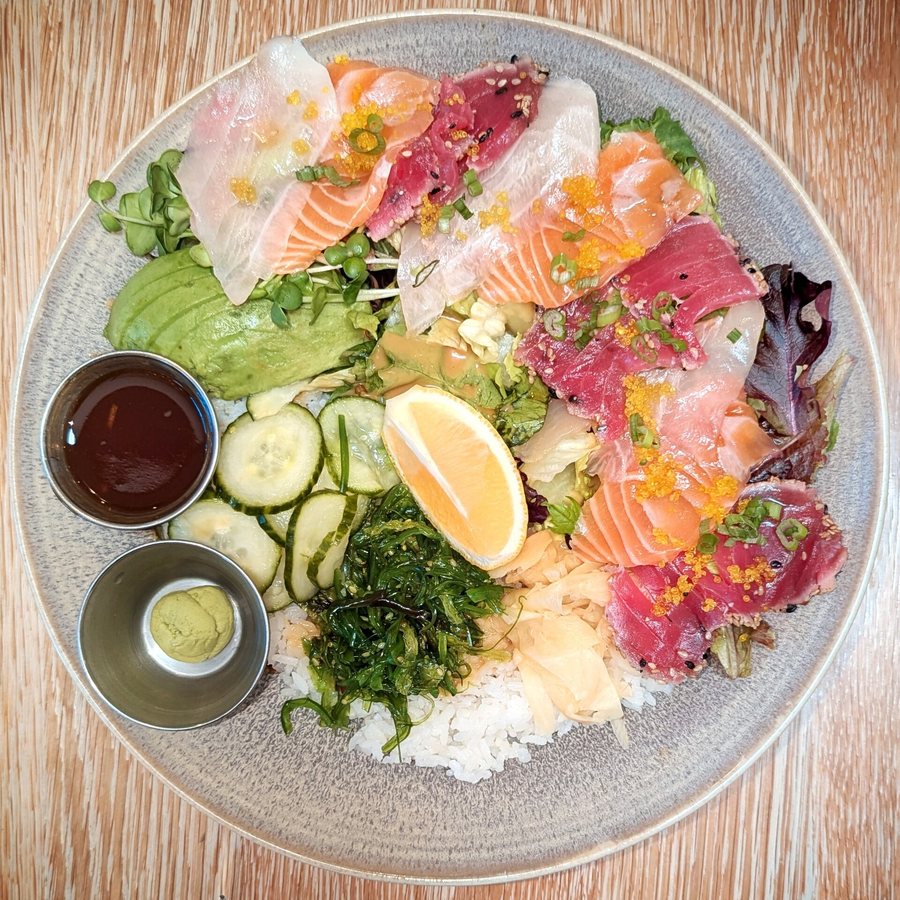 Un bol de riz garni de sashimi, d’algues, d’avocat et de concombre, la sauce soja et le wasabi à côté