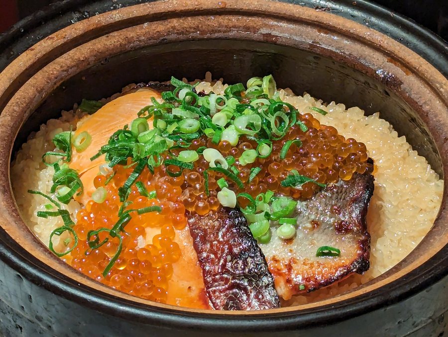 Une cocotte de terre pleine de riz, garnie de saumon grillé, d’œufs de saumon et de cive