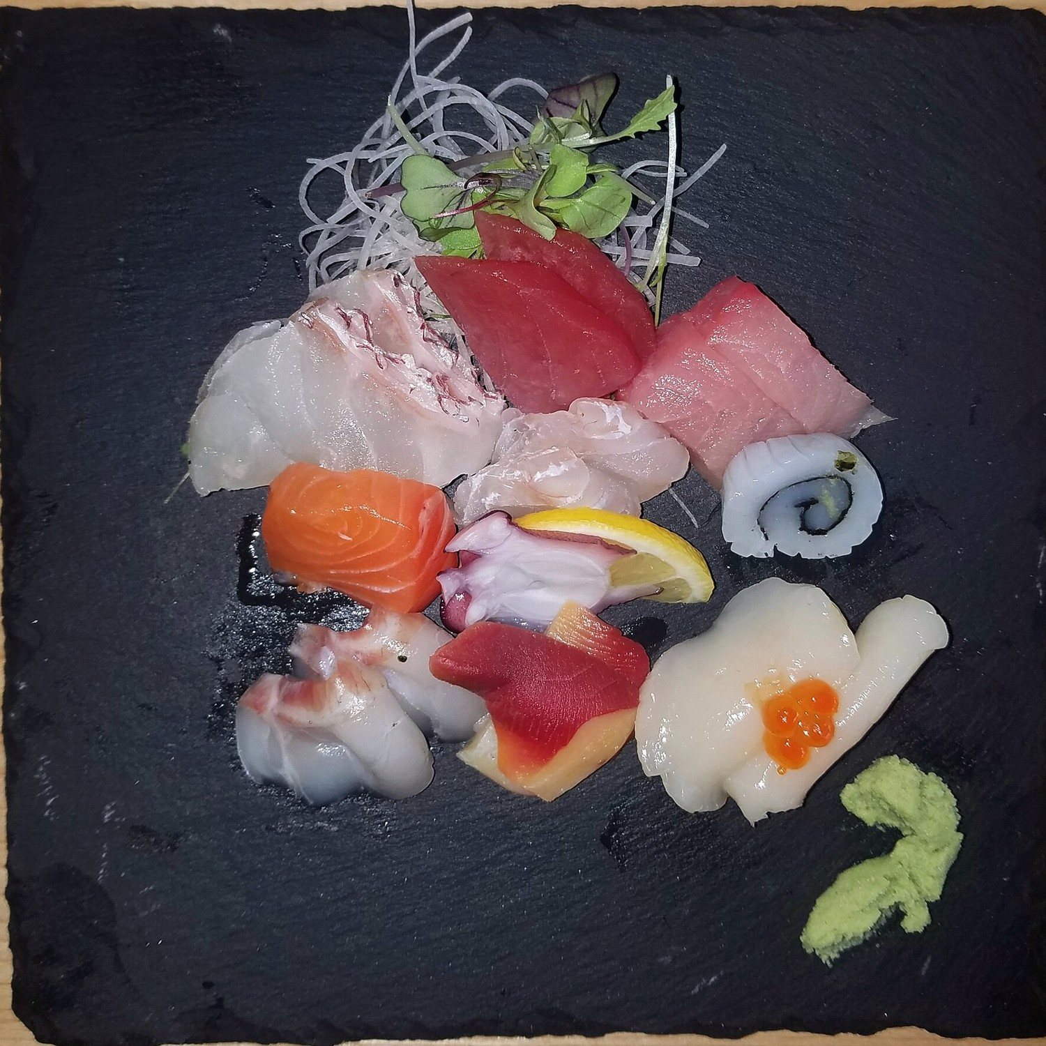 Un assortiment de sashimi sur une ardoise : thon, saumon, daurade, poulpe, saint-jacques, wasabi