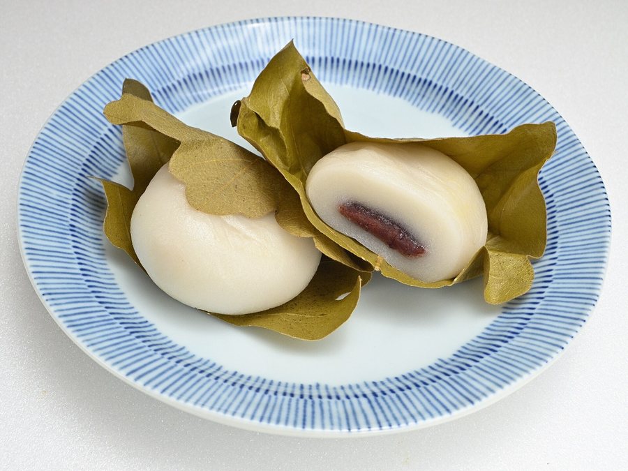 Deux mochi blancs enveloppés de feuilles de chêne, sur une assiette rayée de bleu