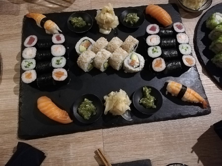Un grand plateau d’ardoise garni de maki, d’uramaki au sésame et de nigiri, gingembre et wasabi en coupelles