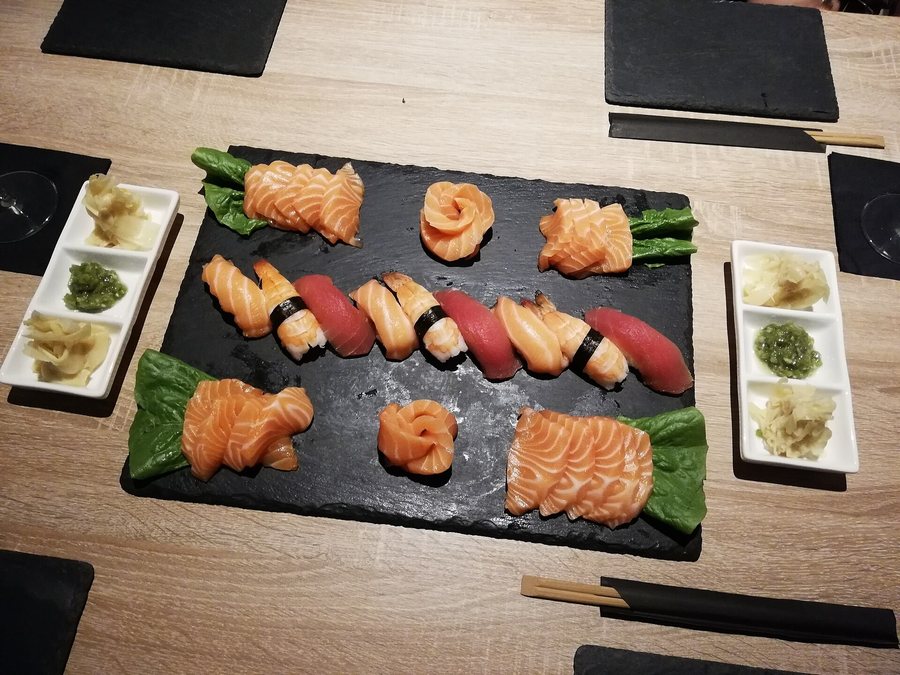 Une ardoise de nigiri et de sashimi de saumon sur une table de bois, gingembre et wasabi de chaque côté