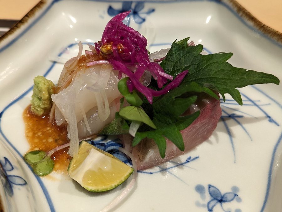 Des tranches de poisson blanc avec une feuille de shiso, du wasabi et un quartier de citron vert