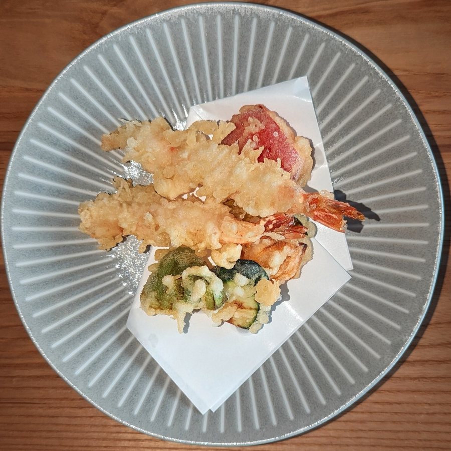 Des crevettes et des légumes en tempura sur un papier, dans une assiette grise